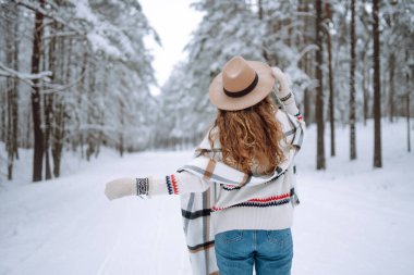 Karlı ağaçların arasında dikilen kadının arka görüntüsü. Gezgin şehveti ve boho stili. Kış tatili.