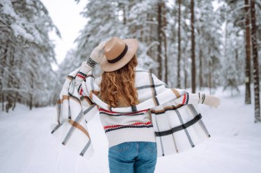 Karlı ağaçların arasında dikilen kadının arka görüntüsü. Gezgin şehveti ve boho stili. Kış tatili.