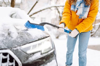 Kışın kar yağarken arabadaki karları fırçayla temizleyen kadın. Buz kazıyorum. Kış temizleme arabası.
