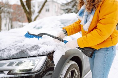 Kışın kar yağarken arabadaki karları fırçayla temizleyen kadın. Buz kazıyorum. Kış temizleme arabası.