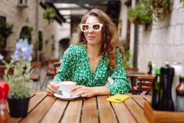 Kafede otururken çay, kahve içen mutlu genç bir kadın. Sokak kafesinde harika vakit geçiriyoruz. İnsanlar, moda, yaşam tarzı, seyahat ve tatiller.