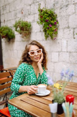 Kafede otururken çay, kahve içen mutlu genç bir kadın. Sokak kafesinde harika vakit geçiriyoruz. İnsanlar, moda, yaşam tarzı, seyahat ve tatiller.