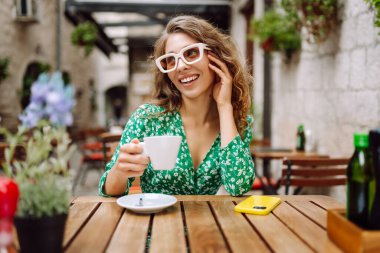 Kafede otururken çay, kahve içen mutlu genç bir kadın. Sokak kafesinde harika vakit geçiriyoruz. İnsanlar, moda, yaşam tarzı, seyahat ve tatiller.