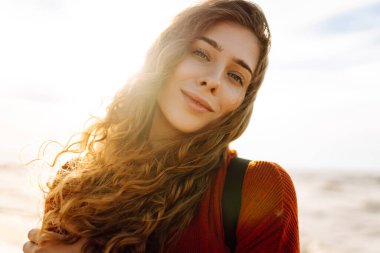 Gün batımında sahilde güzel bir kadının portresi. Soğuk hava. Turist, aktif yaşam tarzı, rahatlama konsepti.
