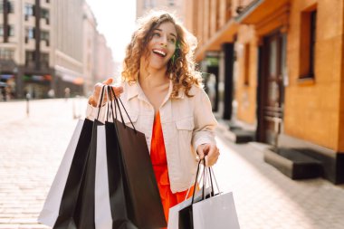Alışveriş çantalı mutlu kadın şehir sokaklarında yürüyor. Tüketim, moda, alışverişler, alışveriş, yaşam tarzı konsepti.