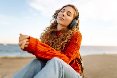 Deniz fenerinin yanında kulaklıkla müzik dinleyen rahat bir kadın. Seyahat, turizm, teknoloji, blog konsepti.