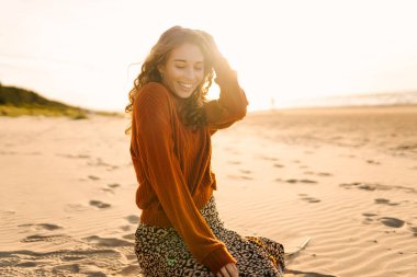 Soğuk ve güneşli havada sahilde güzel kıvırcık bir kadın. Bahar geldi. Yaşam tarzı, seyahat, turizm, doğa, aktif yaşam.