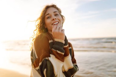 Soğuk ve güneşli havada sahilde güzel kıvırcık bir kadın. Bahar geldi. Yaşam tarzı, seyahat, turizm, doğa, aktif yaşam.