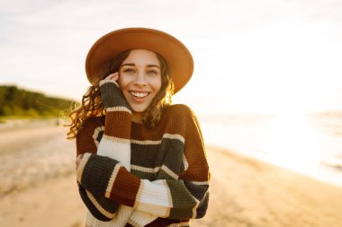 Soğuk ve güneşli havada sahilde güzel kıvırcık bir kadın. Bahar geldi. Yaşam tarzı, seyahat, turizm, doğa, aktif yaşam.