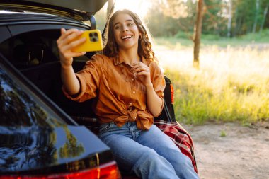Mutlu Kadın arabanın bagajında dinleniyor ve selfie çekiyor. Selfie zamanı. Yaşam tarzı, seyahat, turizm, doğa, aktif yaşam.