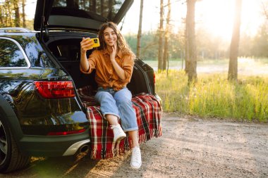 Mutlu Kadın arabanın bagajında dinleniyor ve selfie çekiyor. Selfie zamanı. Yaşam tarzı, seyahat, turizm, doğa, aktif yaşam.