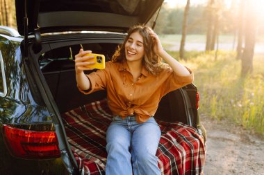 Mutlu Kadın arabanın bagajında dinleniyor ve selfie çekiyor. Selfie zamanı. Yaşam tarzı, seyahat, turizm, doğa, aktif yaşam.