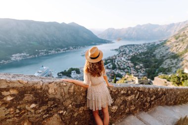 Şapkalı kadın turistin arkadan görünüşü şehrin manzarasına hayran. Yaşam tarzı, tatil, turizm, doğa, aktif yaşam.