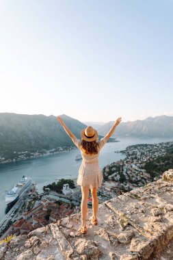 Şapkalı kadın turistin arkadan görünüşü şehrin manzarasına hayran. Yaşam tarzı, tatil, turizm, doğa, aktif yaşam.