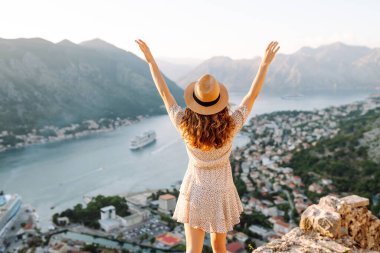 Şapkalı kadın turistin arkadan görünüşü şehrin manzarasına hayran. Yaşam tarzı, tatil, turizm, doğa, aktif yaşam.