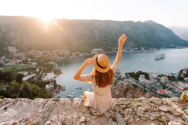 Şapkalı kadın turistin arkadan görünüşü şehrin manzarasına hayran. Yaşam tarzı, tatil, turizm, doğa, aktif yaşam.