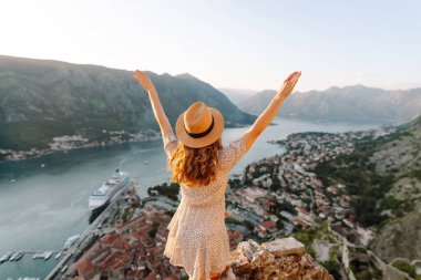 Şapkalı kadın turistin arkadan görünüşü şehrin manzarasına hayran. Yaşam tarzı, tatil, turizm, doğa, aktif yaşam.