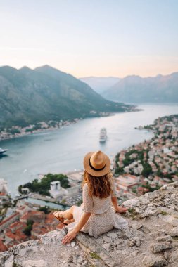 Şapkalı kadın turistin arkadan görünüşü şehrin manzarasına hayran. Yaşam tarzı, tatil, turizm, doğa, aktif yaşam.