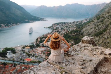 Şapkalı kadın turistin arkadan görünüşü şehrin manzarasına hayran. Yaşam tarzı, tatil, turizm, doğa, aktif yaşam.