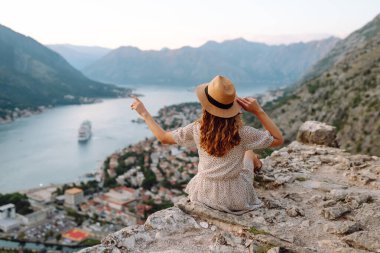 Şapkalı kadın turistin arkadan görünüşü şehrin manzarasına hayran. Yaşam tarzı, tatil, turizm, doğa, aktif yaşam.