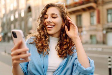 Sokakta elinde telefonla bekleyen güzel bir genç kadının fotoğrafı. Teknoloji kavramı kullan.