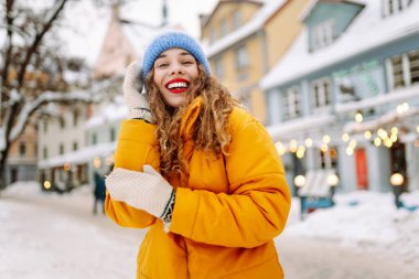 Şenlikli dekorasyon ve ışıklarla süslenmiş genç bir kadın sokakta yürüyor. Moda tarzı. Kış tatili.
