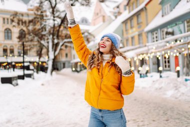 Şenlikli dekorasyon ve ışıklarla süslenmiş genç bir kadın sokakta yürüyor. Moda tarzı. Kış tatili.