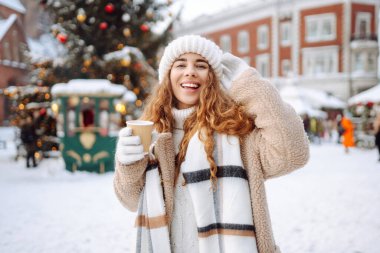 Mutlu kadın Noel pazarında sıcak bir içecek içer. Şenlik ışıklarıyla süslenmiştir. Kış tatili, tatil, turizm konsepti.