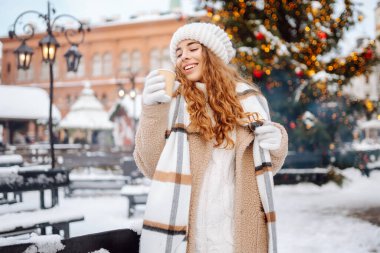 Mutlu kadın Noel pazarında sıcak bir içecek içer. Şenlik ışıklarıyla süslenmiştir. Kış tatili, tatil, turizm konsepti.