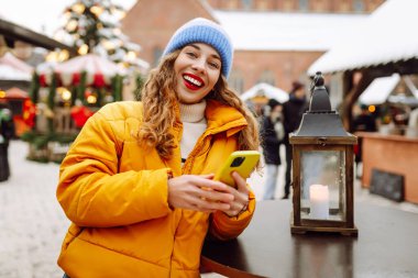 Noel fuarında akıllı telefon kullanan mutlu bir kadın. Kış tatili.