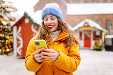 Noel fuarında akıllı telefon kullanan mutlu bir kadın. Kış tatili.