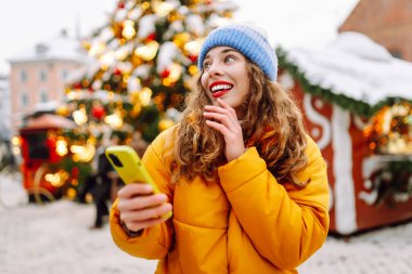 Noel fuarında akıllı telefon kullanan mutlu bir kadın. Kış tatili.