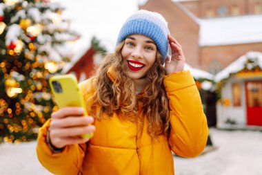 Noel fuarında akıllı telefon kullanan mutlu bir kadın. Kış tatili.