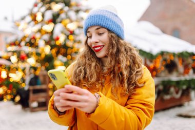Noel fuarında akıllı telefon kullanan mutlu bir kadın. Kış tatili.