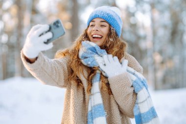 Noel sezonunda seyahat eden mutlu kadın kış ormanlarında karla kaplı ağaçlara ve düşen kara karşı selfie videosu çekiyor..