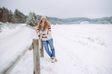 Mutlu kadın, karlı bir ormanda termostan sıcak bir içecek içer. Donmuş kış ormanlarında ısınmak, sıcak eller. Seyahat, gezgin..