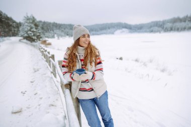 Mutlu kadın, karlı bir ormanda termostan sıcak bir içecek içer. Donmuş kış ormanlarında ısınmak, sıcak eller. Seyahat, gezgin..