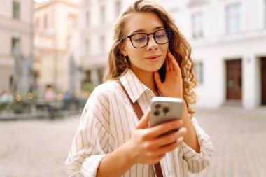 Şehir caddesinde telefonla yürüyen mutlu bir kadın. İletişim, sosyal ağlar, blog yazma, online alışveriş kavramı.