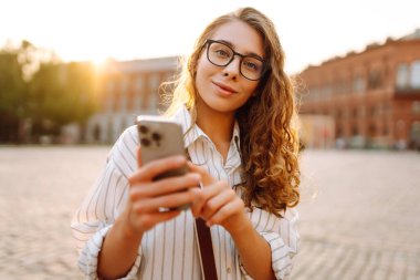 Şehir caddesinde telefonla yürüyen mutlu bir kadın. İletişim, sosyal ağlar, blog yazma, online alışveriş kavramı.