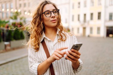 Şehir caddesinde telefonla yürüyen mutlu bir kadın. İletişim, sosyal ağlar, blog yazma, online alışveriş kavramı.