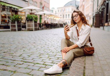 Şehir caddesinde telefonla yürüyen mutlu bir kadın. İletişim, sosyal ağlar, blog yazma, online alışveriş kavramı.