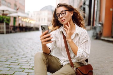 Şehir caddesinde telefonla yürüyen mutlu bir kadın. İletişim, sosyal ağlar, blog yazma, online alışveriş kavramı.