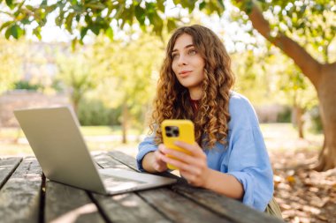 Göl kenarındaki bir kafede dizüstü bilgisayarı ve telefonu olan mutlu bir kadın. İş, blog yazma, serbest çalışma.