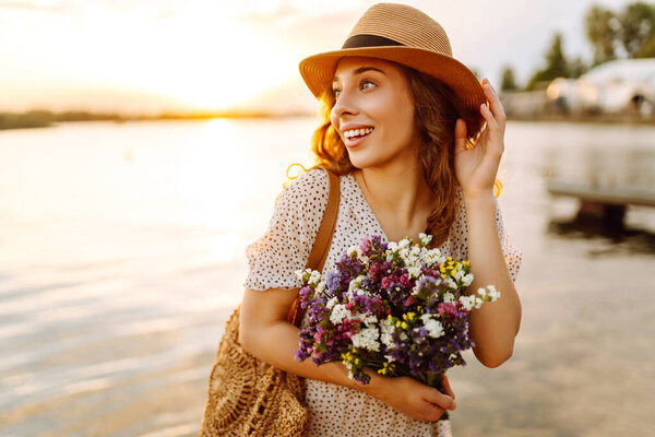 Счастливая женщина в платье сидела на деревянном пирсе у пруда и крепко держала в руке букет полевых цветов. Сельский стиль свадьбы.