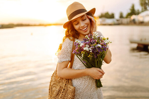 Счастливая женщина в платье сидела на деревянном пирсе у пруда и крепко держала в руке букет полевых цветов. Сельский стиль свадьбы.