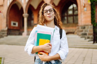 Üniversite yakınlarında çantalı ve kitaplı bir kadın öğrenci. Eğitim, kampüs, arkadaşlık ve insanlar konsepti
