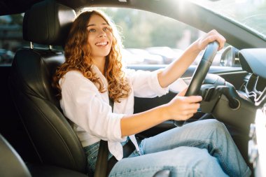 Genç bir kadın güvenli bir şekilde araç kullanıyor, emniyet kemeri takılı. Otomobil yolculuğu.