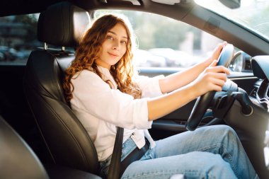 Genç bir kadın güvenli bir şekilde araç kullanıyor, emniyet kemeri takılı. Otomobil yolculuğu.