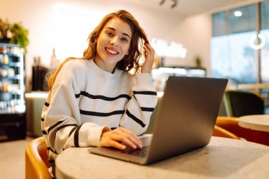 Rahat bir kafede otururken bilgisayarını kullanan serbest çalışan bir kadın. İnternetten alışveriş.