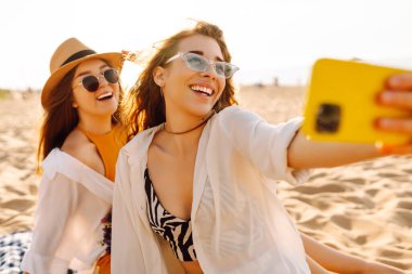Sahilde selfie çeken iki güzel kadın. Pozitif modeller eğleniyor. Seyahat, blog, hafta sonu, rahatlama ve yaşam tarzı konsepti.